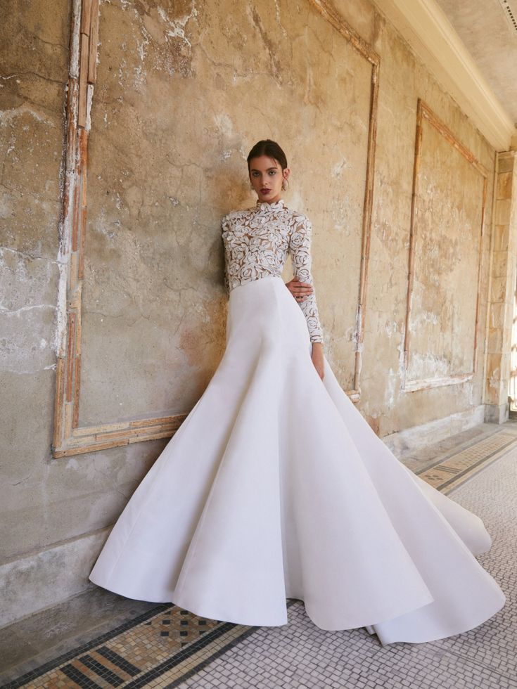 a woman in a white wedding dress leaning against a wall with her hands on her hips