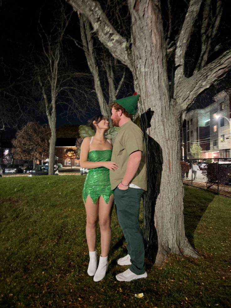 a man and woman dressed up as tinkerbells standing next to a tree