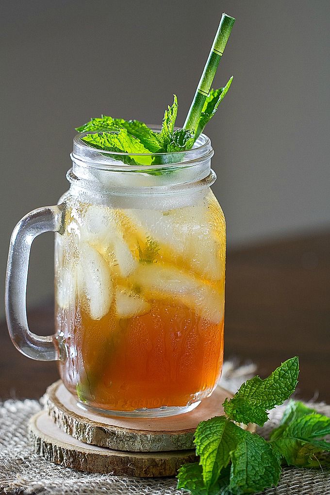 a mason jar filled with iced tea and mint leaves on a tablecloth next to a glass of water