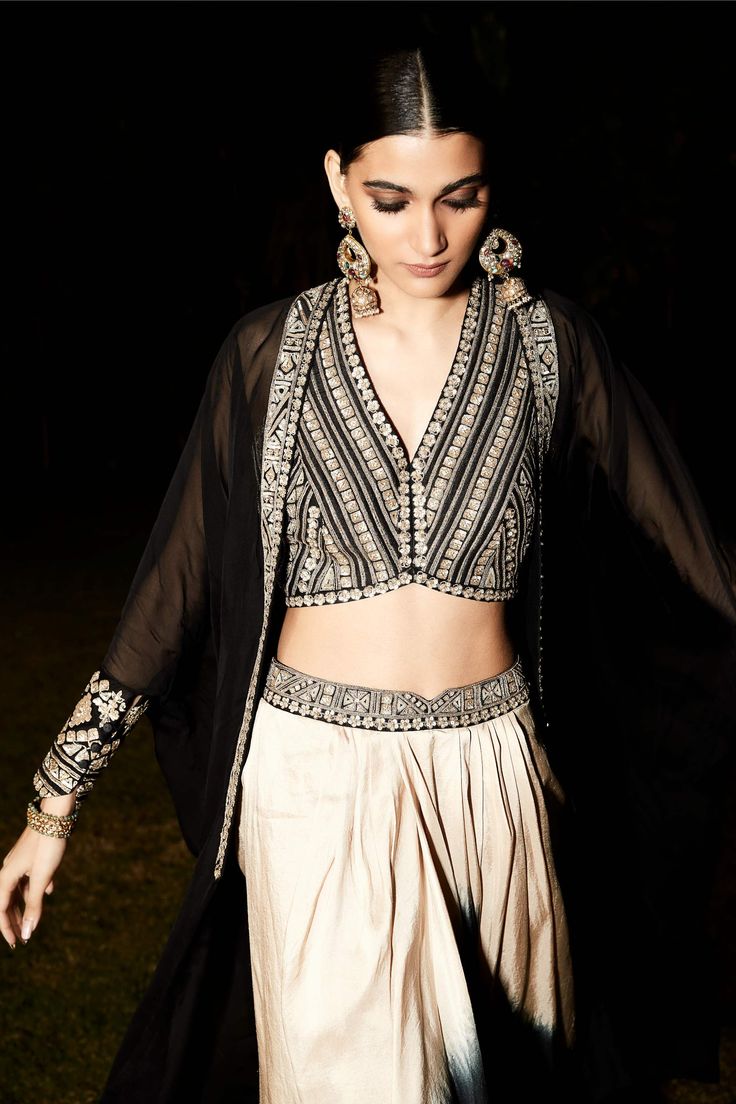 Editor's Note Featuring a black cape with tarnished silver vintage zardozi embroidery in Aztec and flora inspired artworks on the border and cuffs. Comes with blouse with a greako-roman embroidery and ombre draped skirt. Fabric: Organza georgette Color: Black Neckline: V neck Component: Cape, blouse and skirt Occasion: Festive Disclaimer: Product colour may slightly vary due to photographic lighting sources Care: Dry Clean Only About the Designer Matsya by Utkarsh Ahuja curated for the princess Traditional Sharara With Cape Sleeves, Festival Embroidered Choli With Cape Sleeves, Bohemian Party Sets With Cape Sleeves, Traditional Sharara With Cape Sleeves For Festivals, Traditional Lehenga With Embroidered Cape Sleeves, Traditional Sharara With Mirror Work And Cape Sleeves, Traditional Choli With Cape Sleeves For Designer Wear, Black Embroidered Sharara For Evening, Traditional Designer Choli With Cape Sleeves