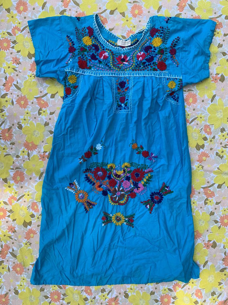 Boho Blue Embroidered Dress Made in Mexico 100% cotton Blue dress with multi-color embroidered floral patterns Measures: 42" length 4.5" sleeve 22" pit to pit (B12) Blue Cotton Floral Print Dress, Traditional Blue Dress With Embroidered Hem, Traditional Blue Embroidered Dress With Embroidered Hem, Blue Cotton Dresses With Short Sleeves, Traditional Blue Dress With Embroidered Neckline, Blue Embroidered Dress For Spring, Blue Embroidered Dress With Neckline Detail For Spring, Short Sleeve Cotton Embroidered Beach Dress, Short Sleeve Embroidered Cotton Dress For Beach