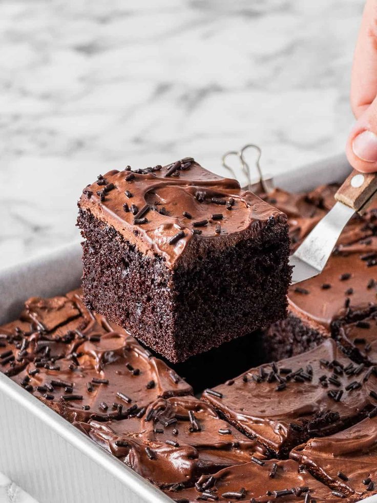 someone cutting into a piece of chocolate cake on top of a pan with frosting