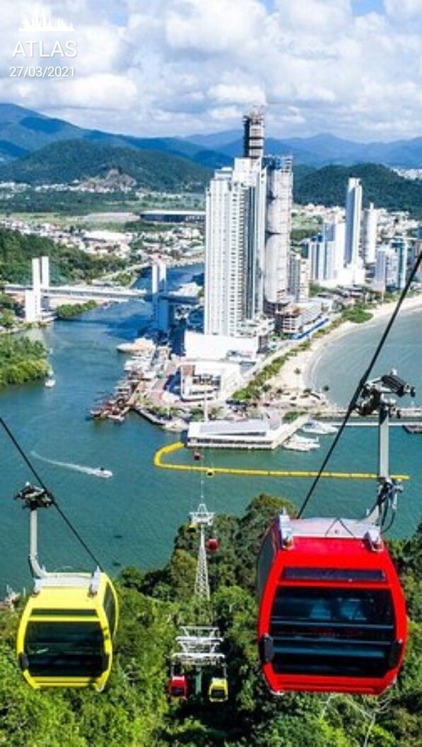 two red and yellow gondola cars going over the water in front of a city