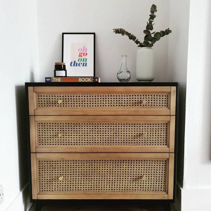 a wooden dresser sitting next to a wall with a vase on top of it and a plant in the corner