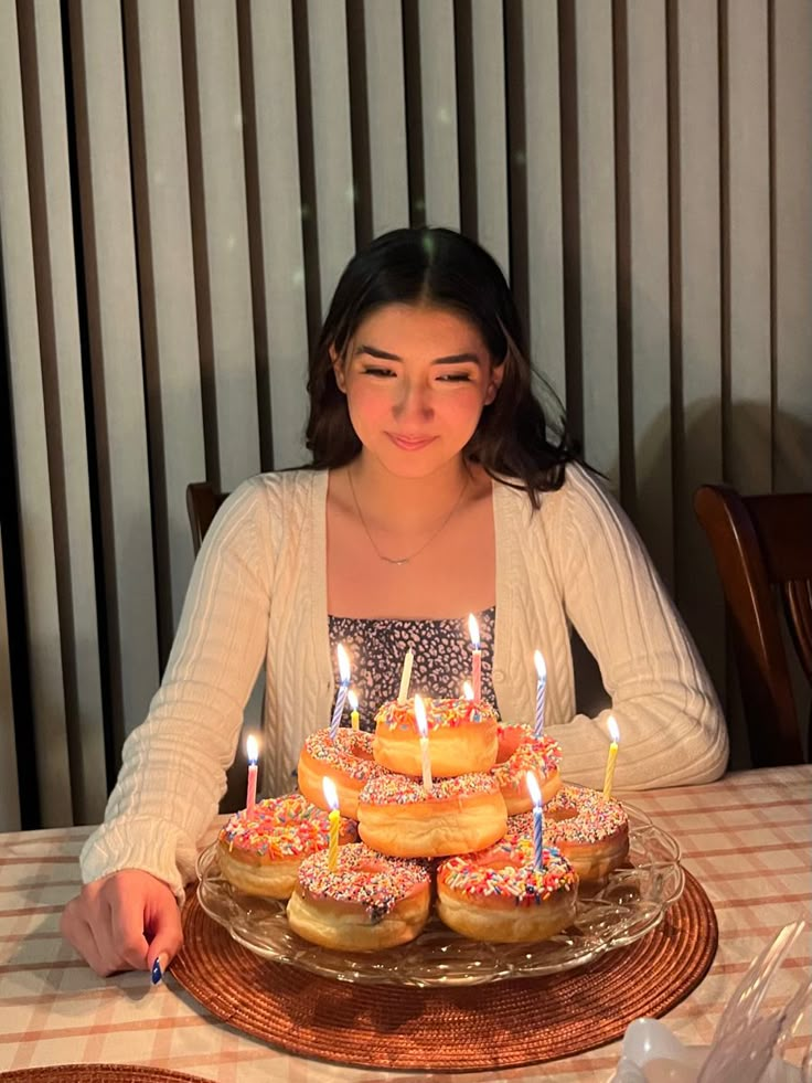 a woman sitting at a table in front of a cake with donuts on it