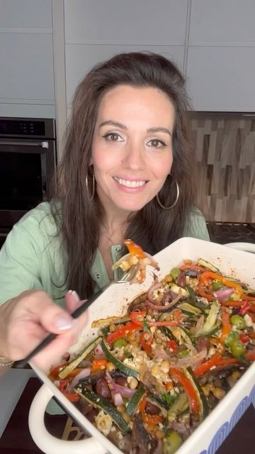 a woman is holding up a casserole dish with vegetables in it and smiling at the camera