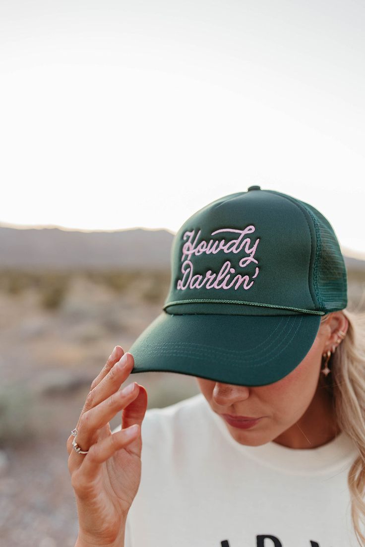 Say hello to the perfect summer accessory with our Howdy Darlin' Trucker Hat! Made with a classic trucker design, this green hat features "Howdy Darlin'" embroidered on the front. Keep cool and stylish all summer long with this trendy hat! Paired with THE HOLD YOUR HORSES GRAPHIC TEE IN IVORY, THE 90'S FLARE JEANS IN BLACK BY VERVET, and THE MIMI COWGIRL BOOTS IN WHITE. Howdy Darlin' embroidered on front in pink Trucker style Adjustable snapback 100% polyester Due to sanitary reasons, accessorie Green Adjustable Trucker Hat With Curved Bill, Adjustable Green Trucker Hat With Curved Bill, Trendy Green Baseball Cap For Outdoor, Green Baseball Cap With Curved Bill For Summer, Spring Green Trucker Hat With Curved Bill, Spring Green Trucker Baseball Cap, Green Trucker Baseball Cap For Spring, Green Curved Bill Baseball Cap For Summer, Green Curved Bill Trucker Hat For Spring