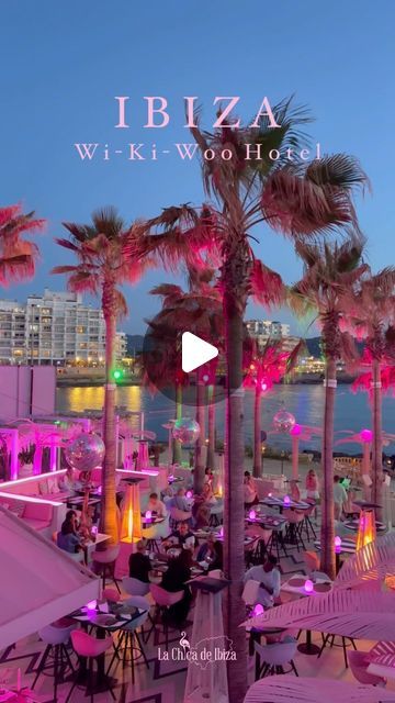 the beach is lit up with pink lights and palm trees, while people sit at tables under umbrellas