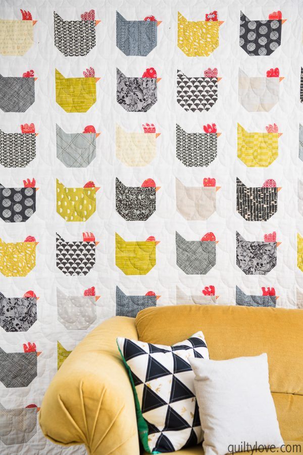 a yellow couch sitting in front of a quilted chicken wall hanging on the wall