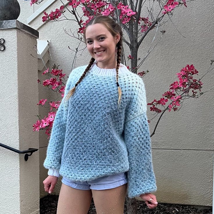 a woman standing in front of a tree wearing short shorts and a blue knitted sweater