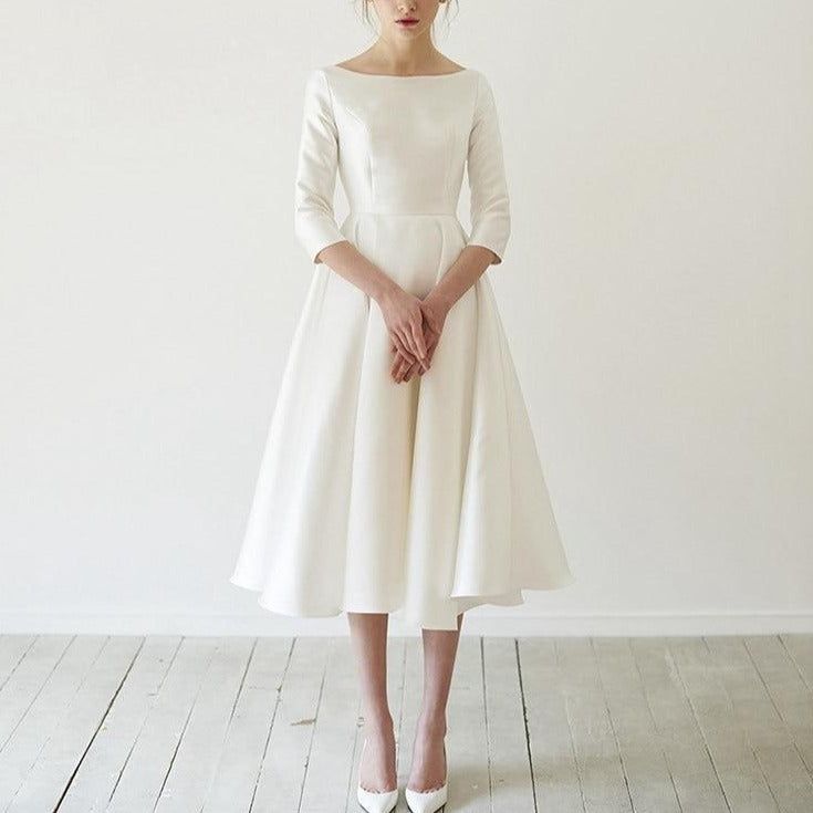 a woman standing in front of a white wall wearing a dress with long sleeves and high heels