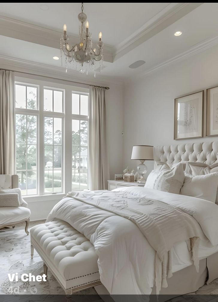 a large white bed sitting in a bedroom next to two chairs and a chandelier