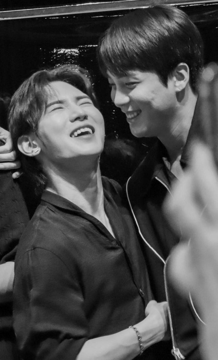 two young men are smiling and having fun together in black and white, one is holding his arm around the other's neck