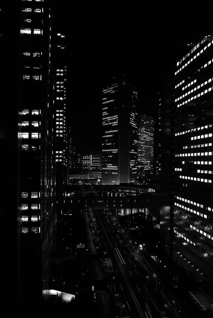 black and white photo of city at night with lights in the windows, cars passing by