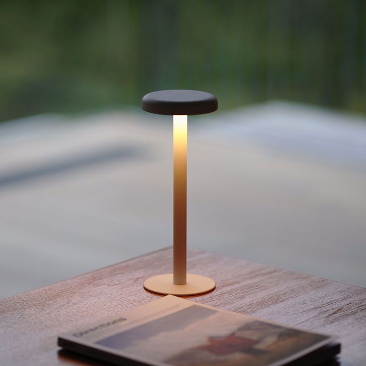 a table lamp sitting on top of a wooden table next to a book and magazine