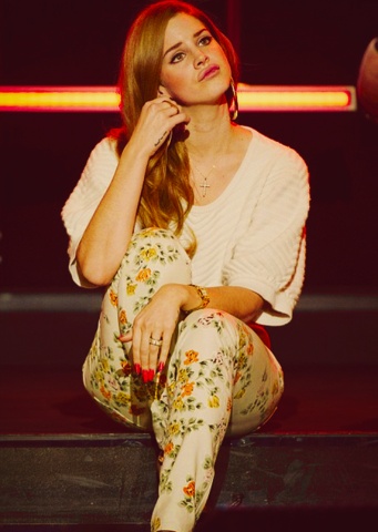 a woman sitting on top of a wooden floor next to a red neon sign in the background