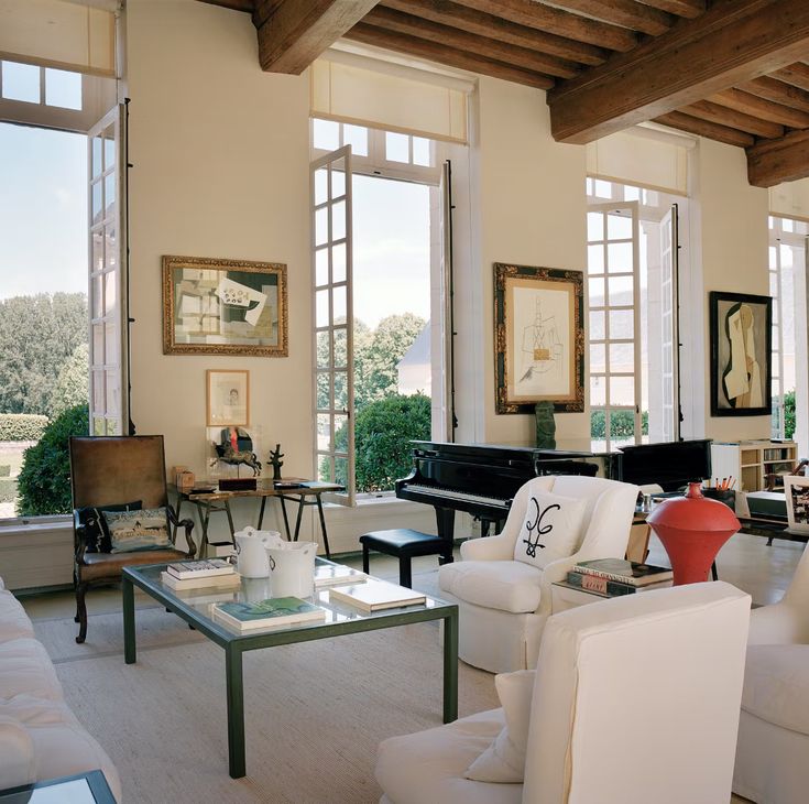 a living room filled with lots of white furniture and large windows covered in wood beams