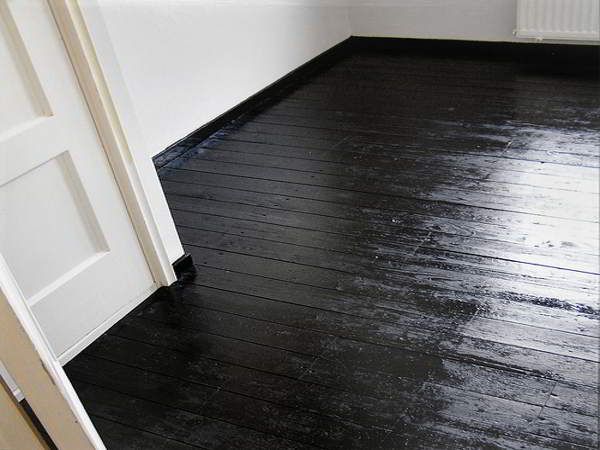 an empty room with black wood floors and white walls is seen in this image from the doorway