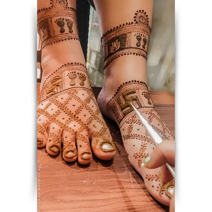 two feet with henna tattoos on them and one hand holding a nail polisher