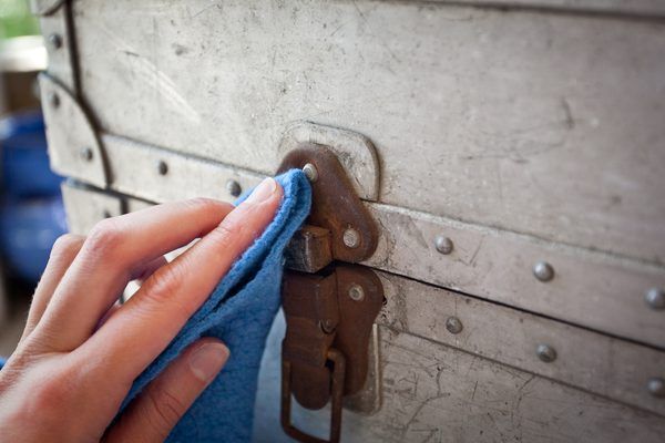 a person wiping up an old trunk with a blue towel and some metal rivets