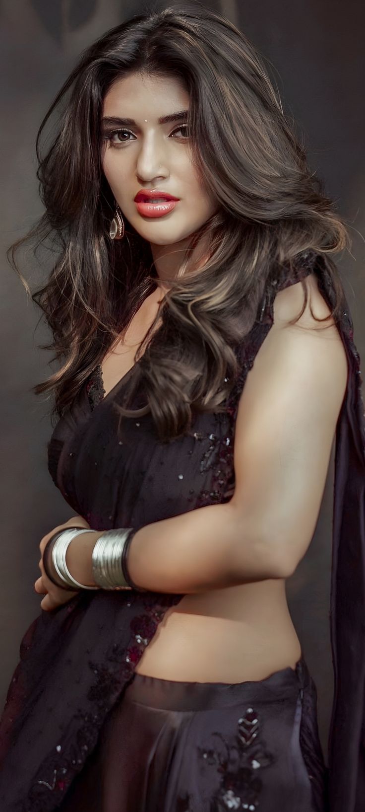 a woman with long hair wearing a black dress and bracelets, posing for the camera