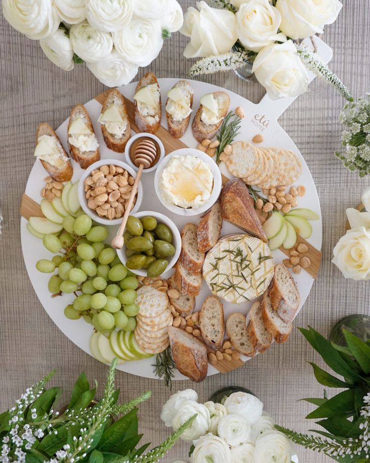 a platter filled with cheeses, crackers and nuts next to white flowers