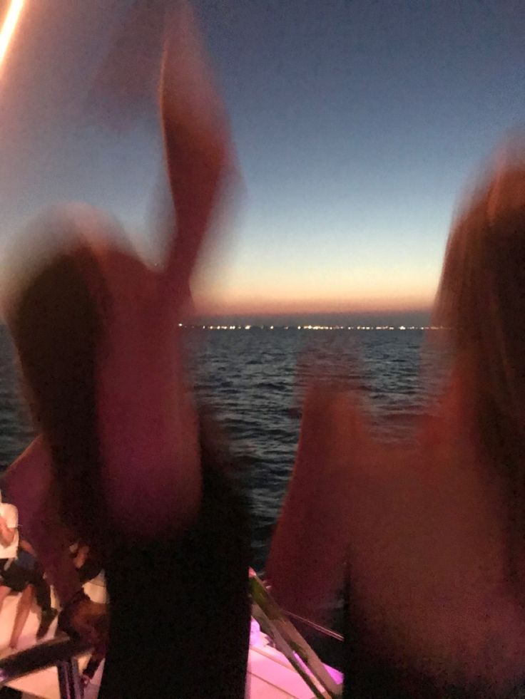 two people are sitting on a boat in the water at night with their hands up