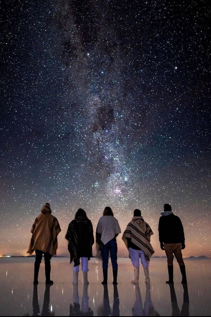 four people looking up at the stars in the night sky with their backs to the camera