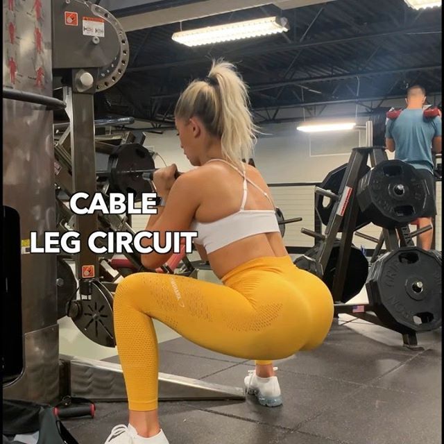 a woman squats on the ground in front of a gym machine with an inscription that reads cable leg circuit