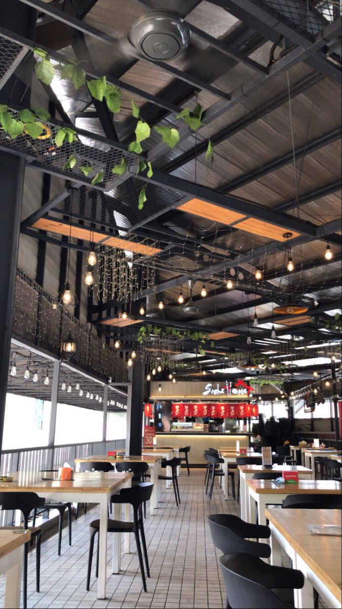 an empty restaurant with lots of tables and hanging plants on the ceiling above them,