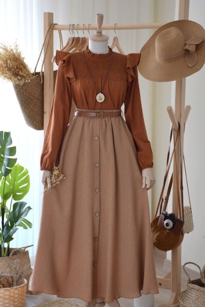 a dress and hat are hanging on a rack in front of a potted plant