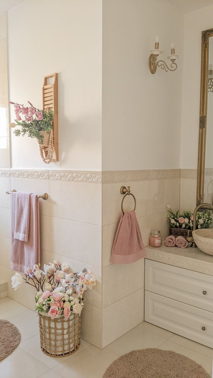 a white bathroom with pink towels hanging on the wall and a basket full of flowers