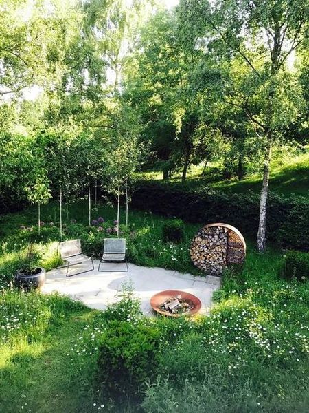 an outdoor patio with chairs and fire pit surrounded by greenery, shrubs and trees