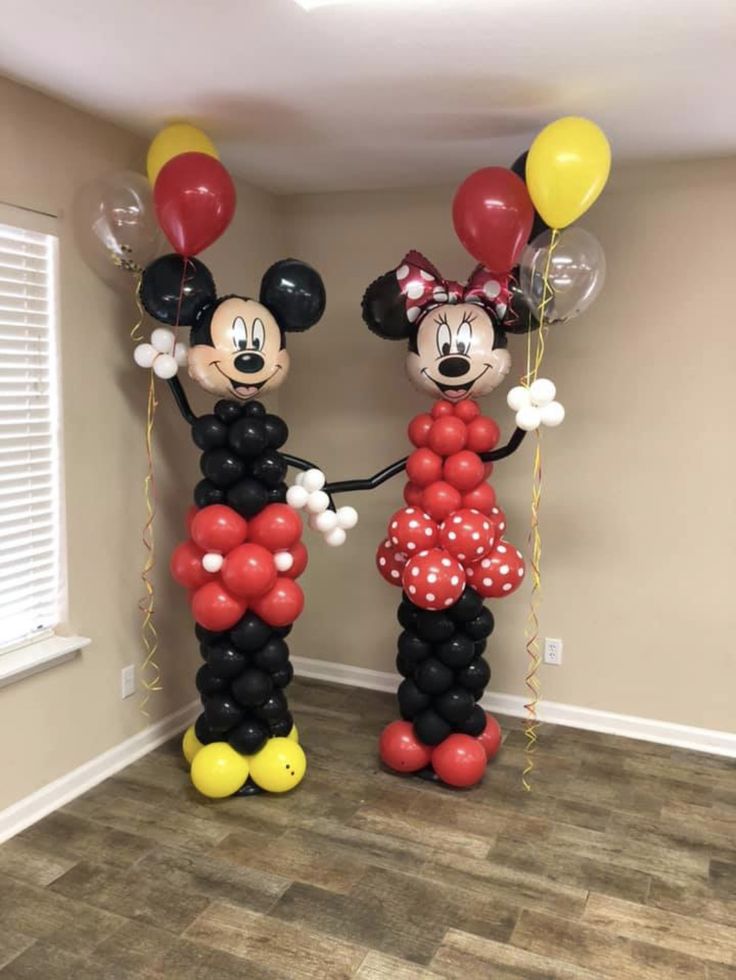 two mickey and minnie mouse balloons are standing next to each other in an empty room