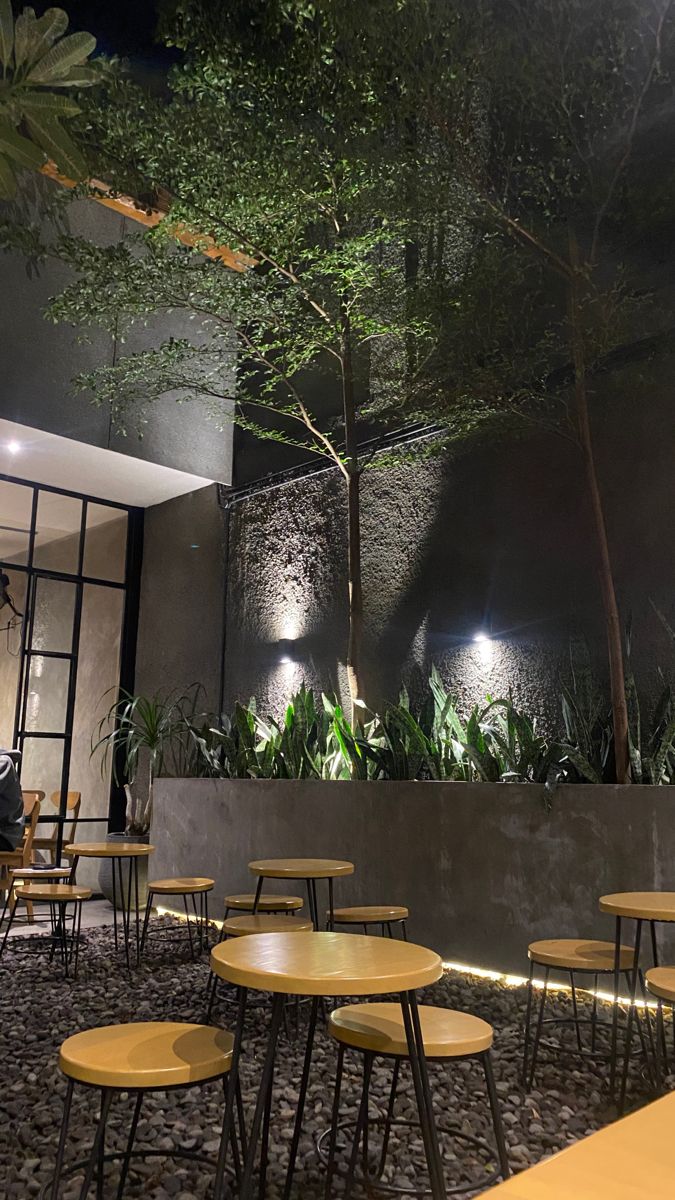 tables and chairs are lined up in front of a wall with plants on it at night