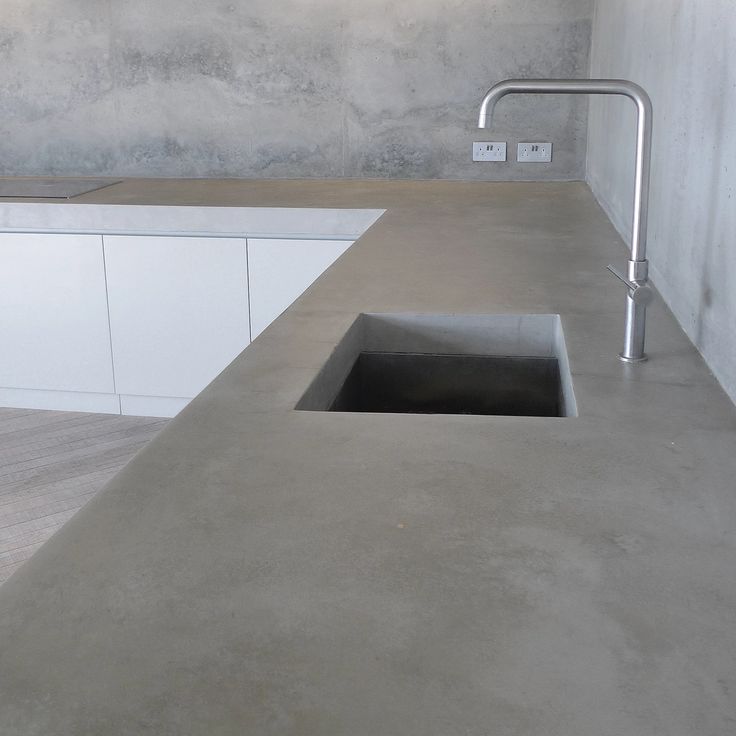 a concrete counter top with a sink and faucet in the middle, against a wall