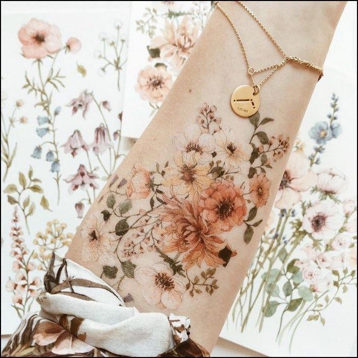 a woman's arm with flowers on it and a gold disc charm hanging from the wrist