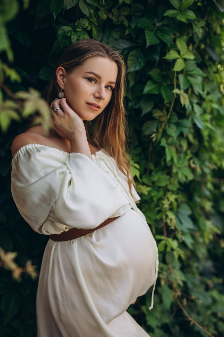 a pregnant woman poses in front of greenery