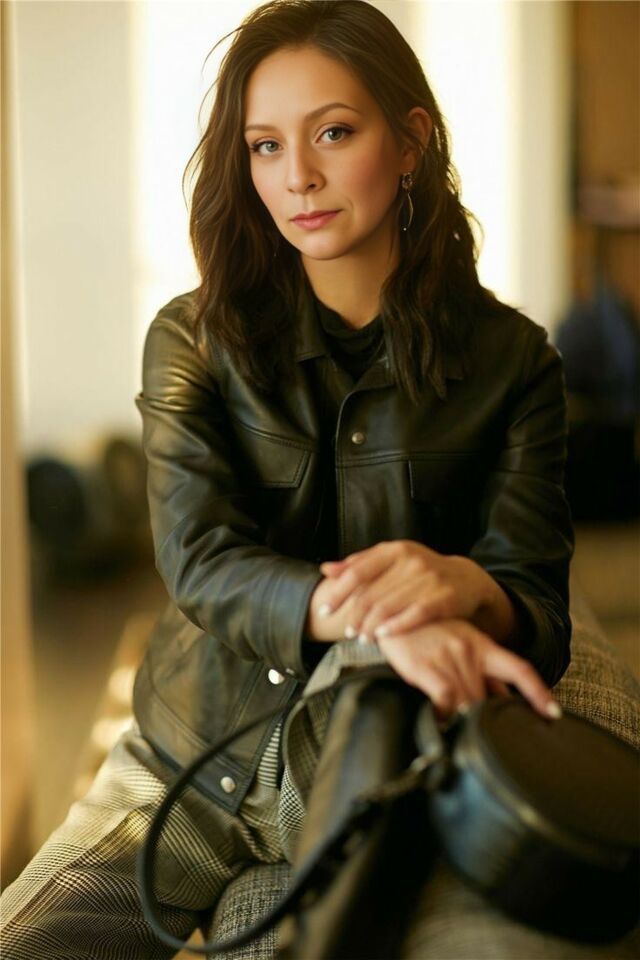 a woman sitting on top of a couch wearing a black jacket and holding a purse