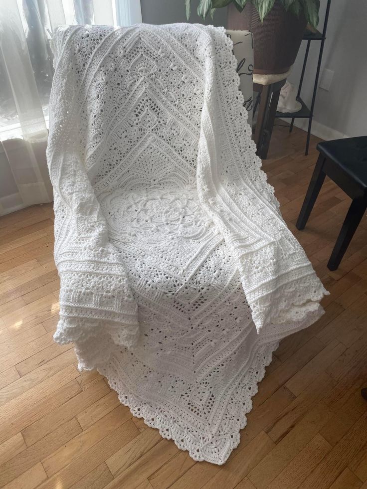 a white crocheted blanket sitting on top of a wooden floor next to a window