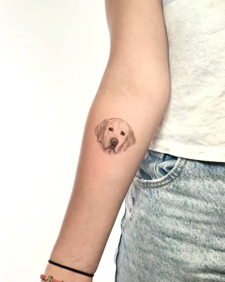 a woman's arm with a small dog tattoo on the left side of her arm