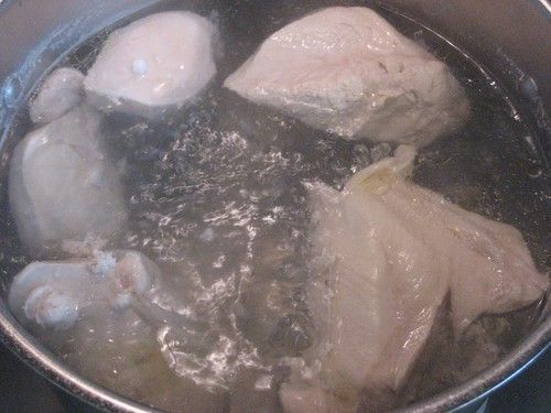 raw chicken being cooked in a pot on the stove top with boiling water and ice