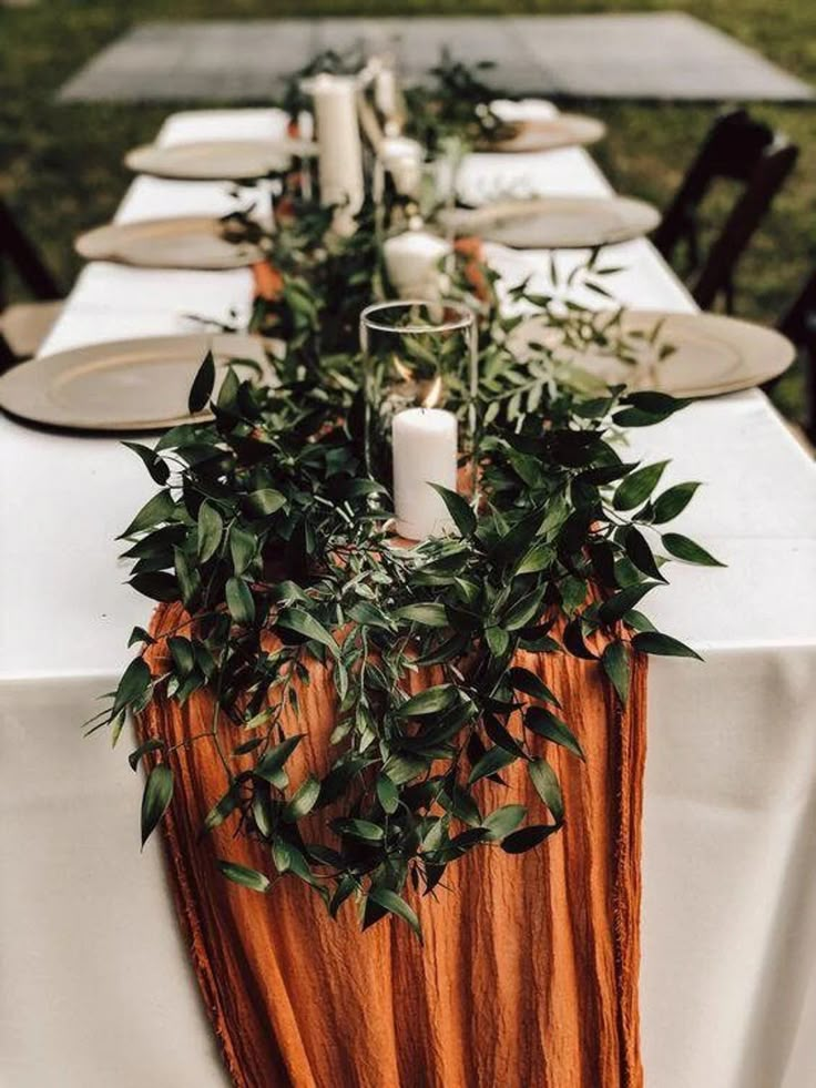 a long table with candles and greenery is set up for an outdoor dinner party