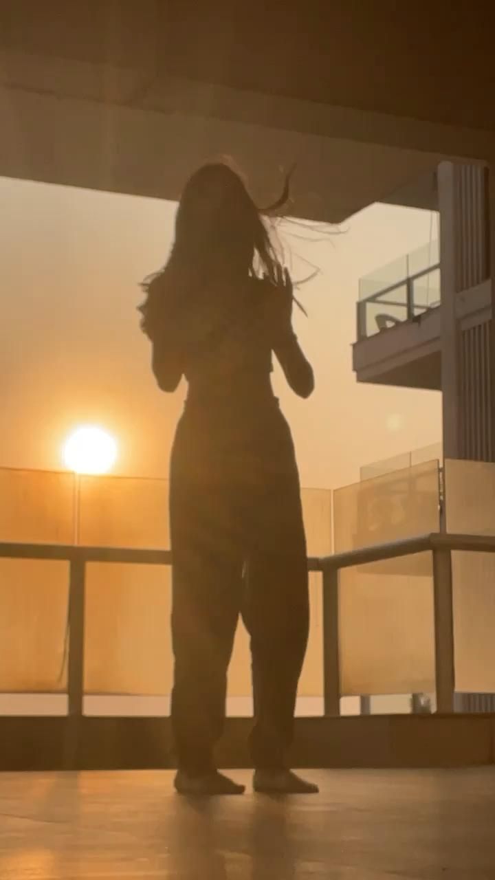 a woman standing on top of a roof next to a tall building at sunset with her hair blowing in the wind