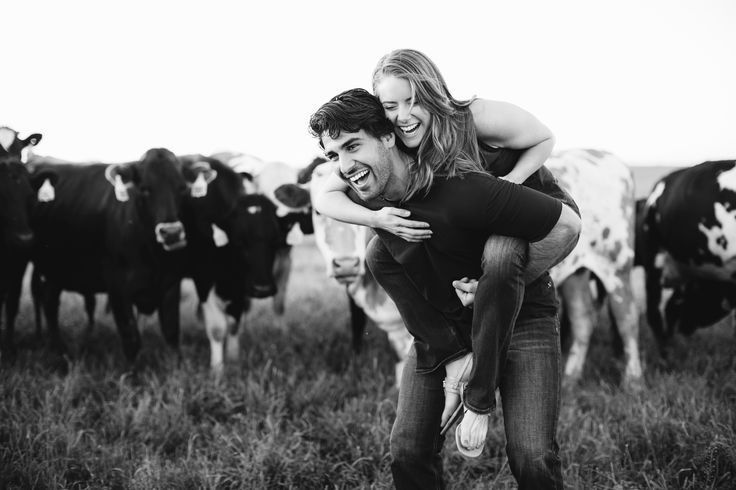 a man carrying a woman on his back in front of cows