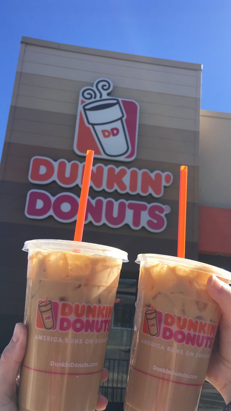 two people holding up drinks in front of dunkin donuts