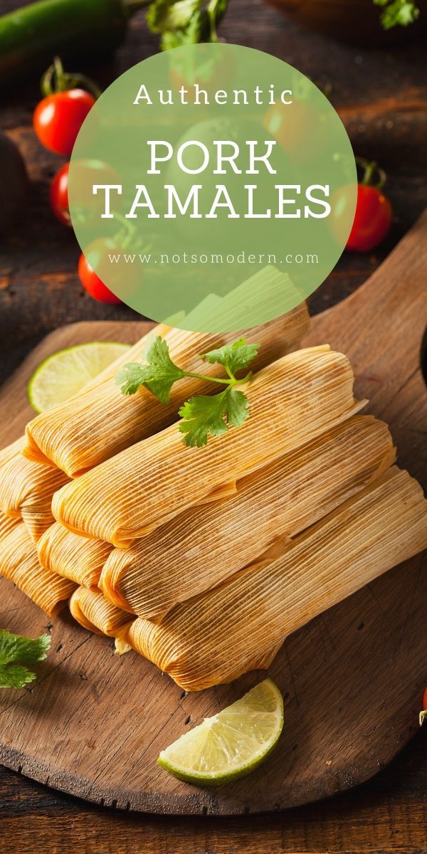 some tamales on a cutting board with limes and tomatoes