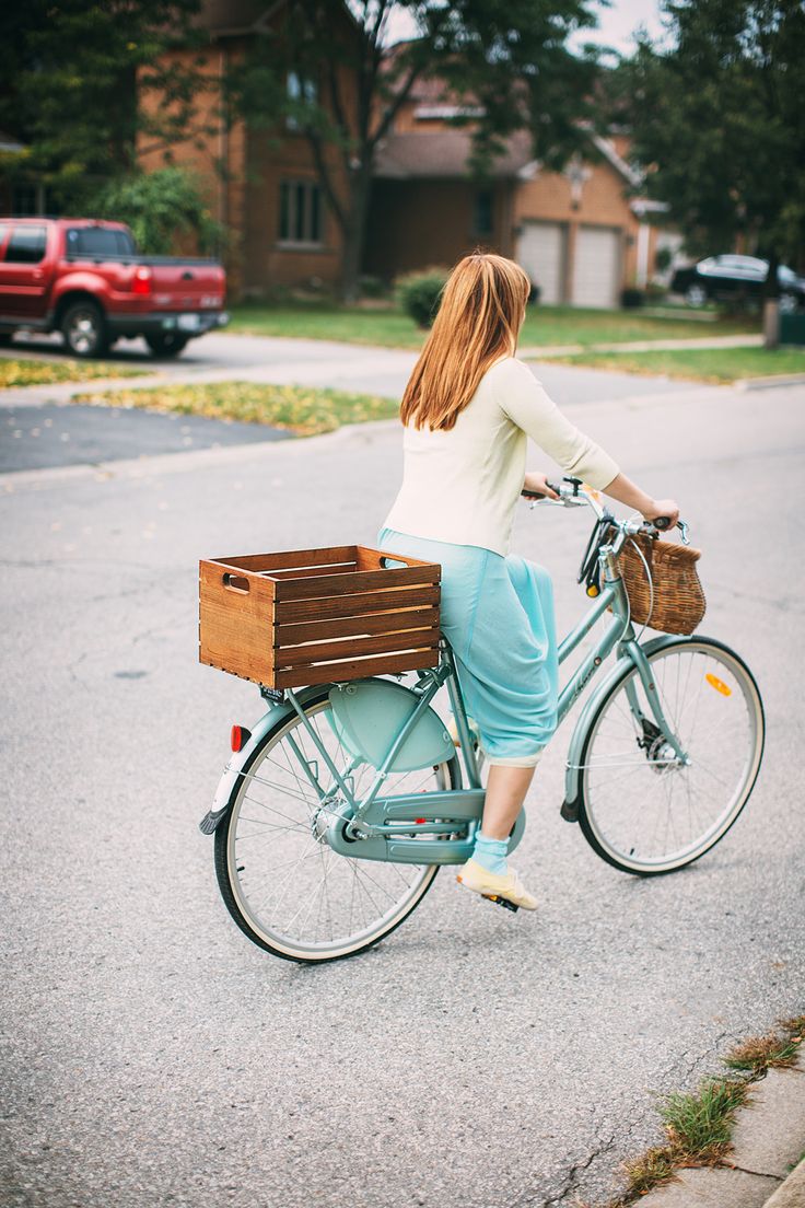 the woman is riding her bike down the street with a basket on it's back