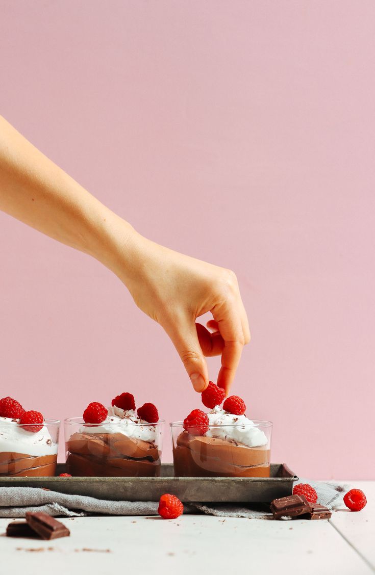 a person placing raspberries on top of desserts