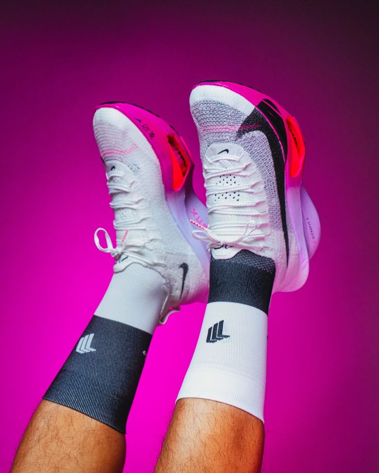 the feet of a person wearing white and black tennis shoes with pink lighting behind them